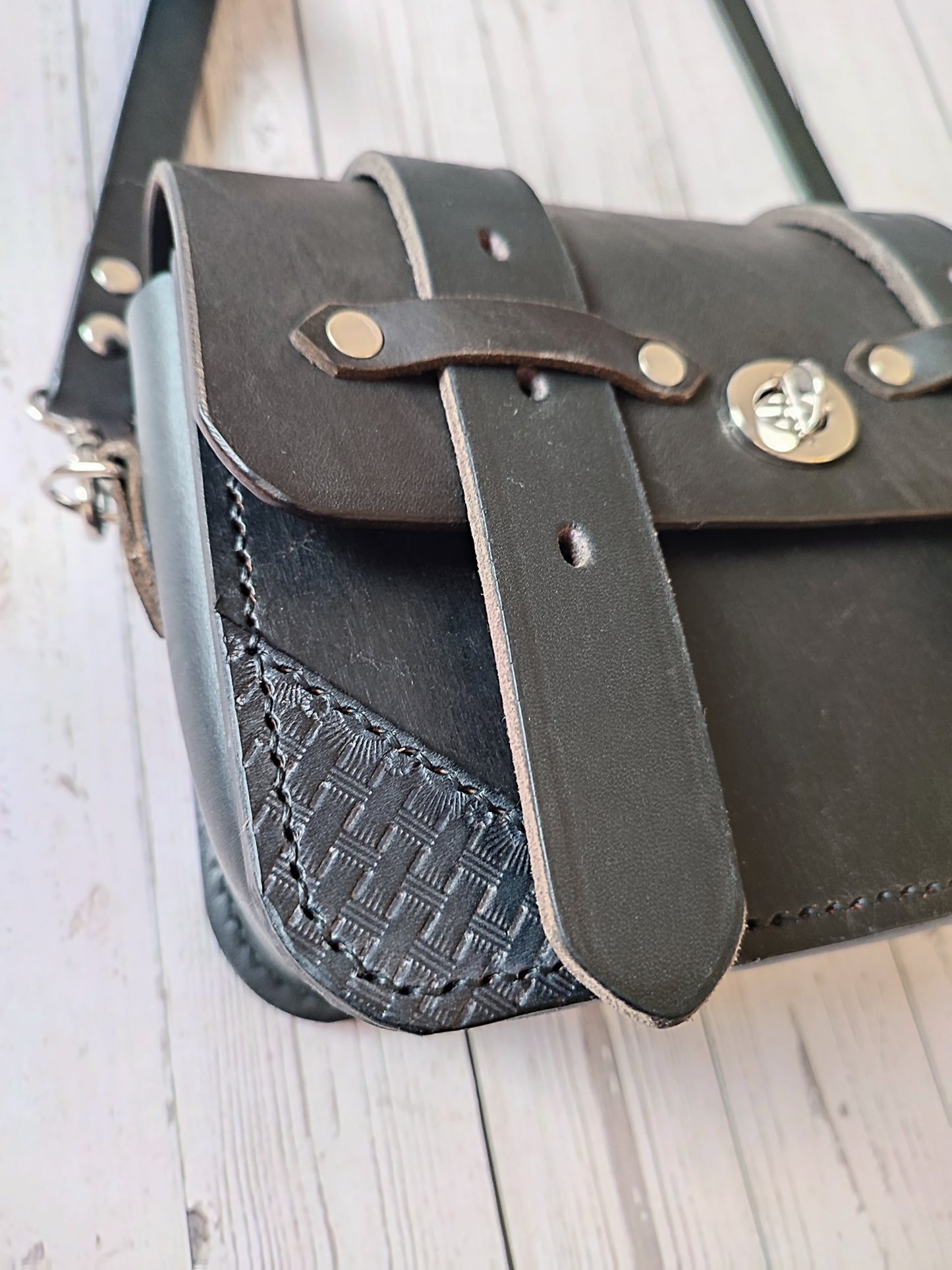 Détails du sac besace noir au style western avec du cuir sculpté à la main et des sanglons de selle.