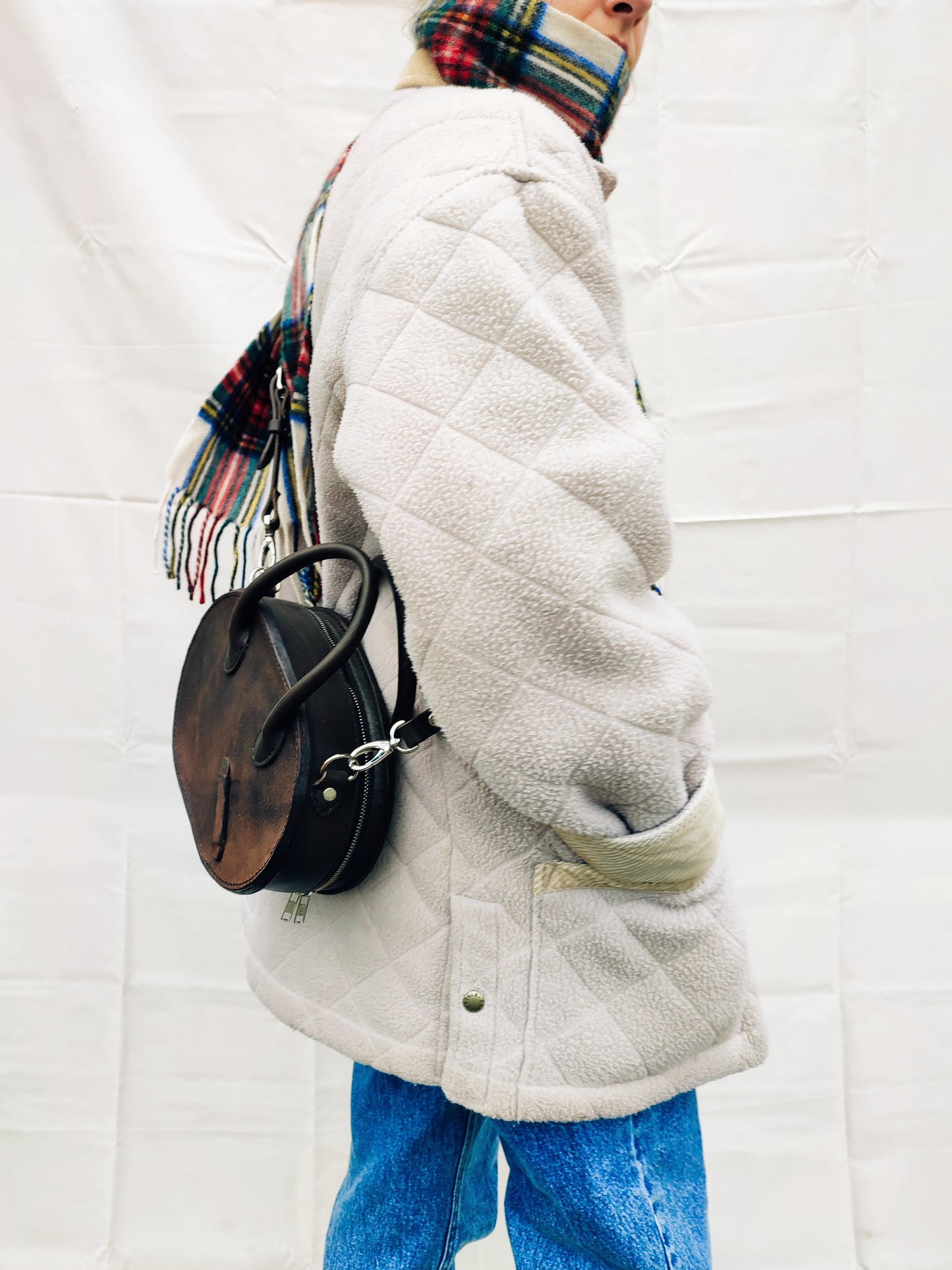 Le sac Oval en cuir de selle d'équitation porté par une femme emmitouflée dans un manteau chaud et une écharpe au motif tartan.