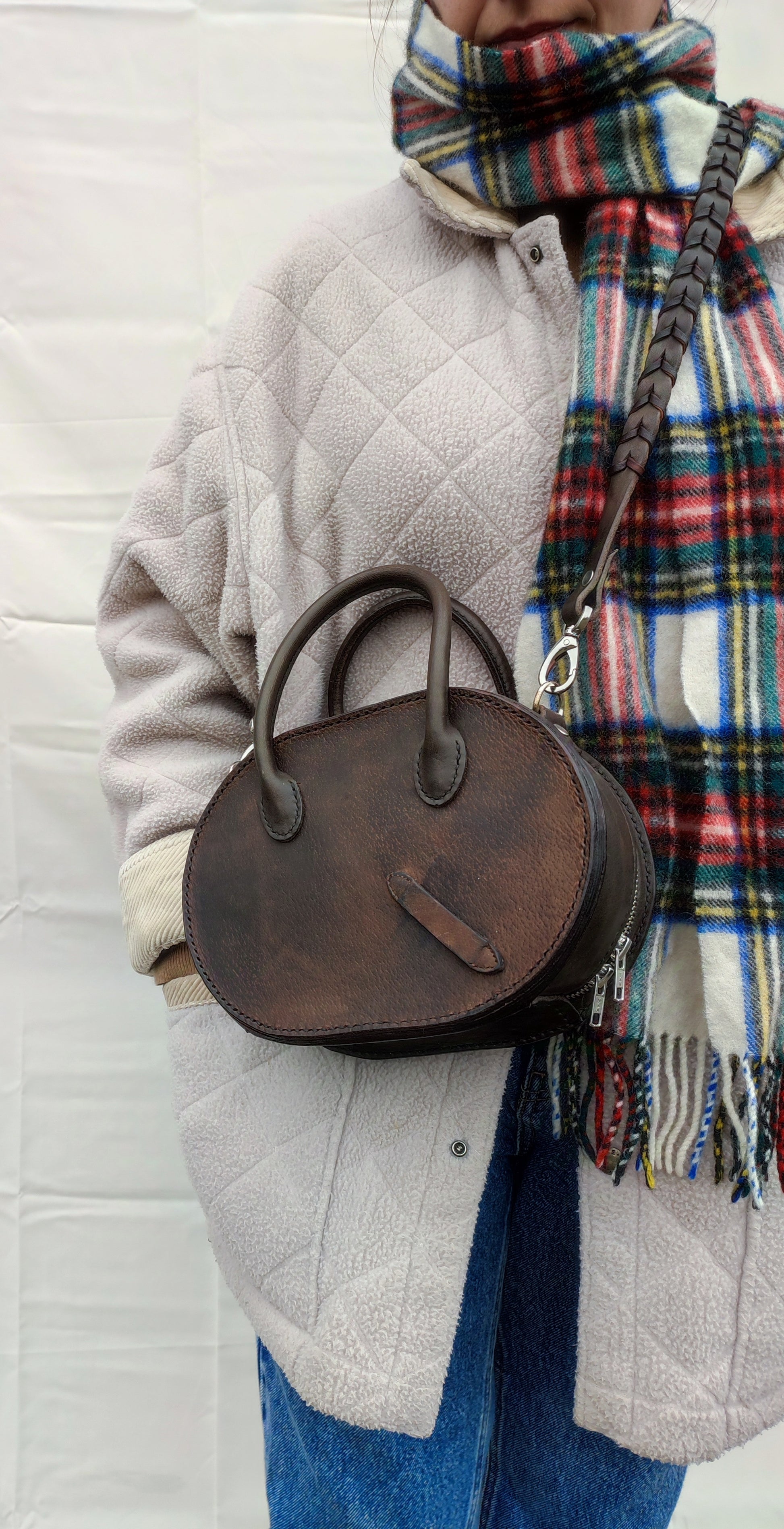 Le sac Oval en cuir marron patiné par le temps avec une bandoulière fait en rêne bredies pour un style très cavalier. 