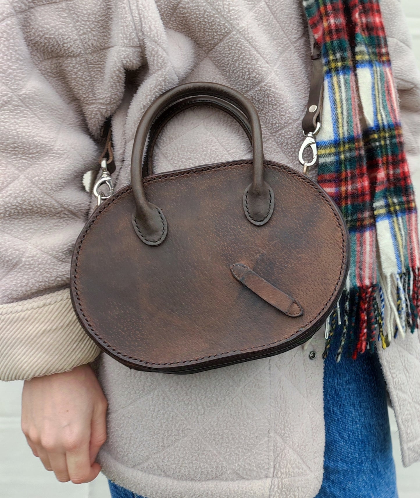 Vu de face du sac Oval en cuir marron fabriqué à partir d'un quartier de selle. On peut voir le détail du passage d'étrivière. 