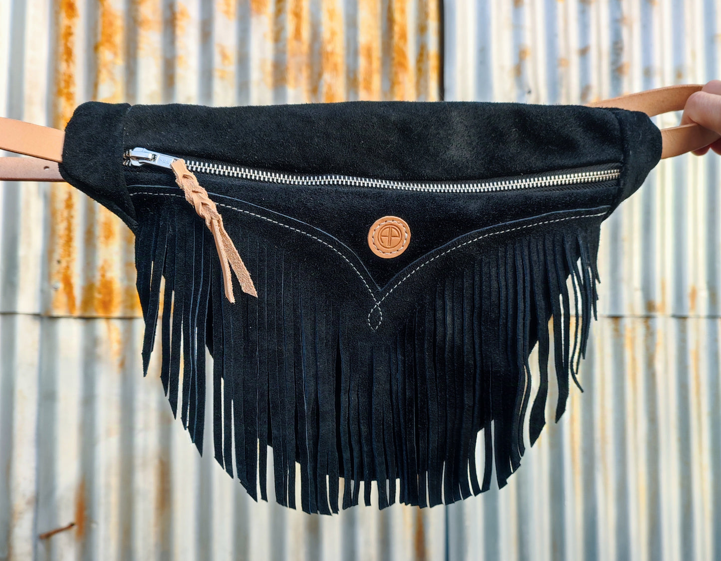 Sac banane à franges style western en croûte de cuir noir. Fermeture éclaire et logo AP cuir clair.