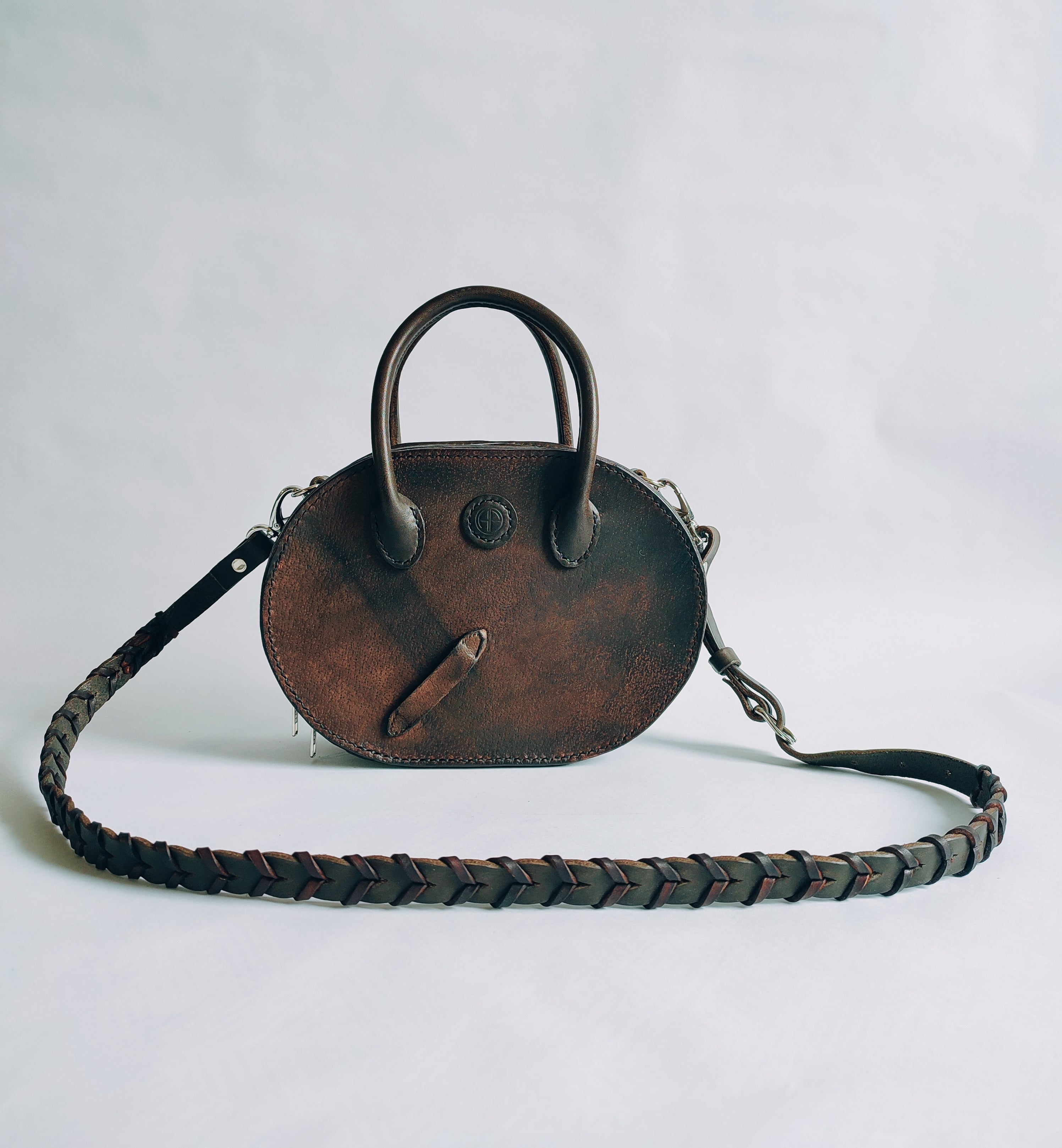 Le sac Oval vu de face montre un design à la fois moderne et rustique avec le détail du cuir patiné et le passage d'étrivière.