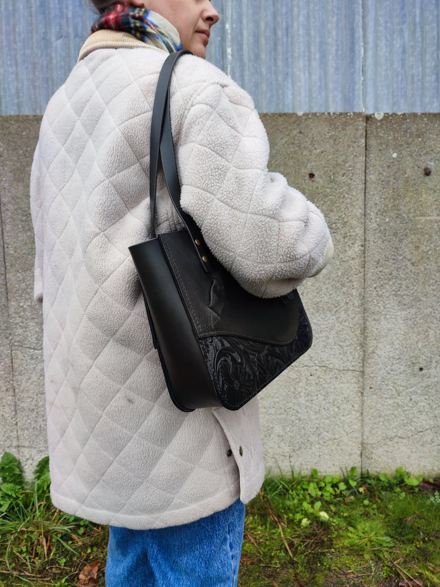 Vue du tote bag bag en cuir de selle noir porté à l'épaule par une femme cavalière en civil.