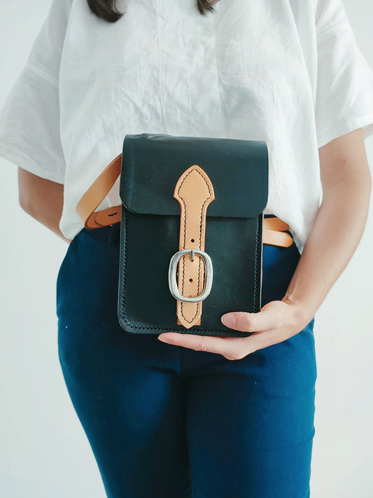 La sacoche Grands Quartiers vu de face et tenue dans la main d'une femme cavalière.