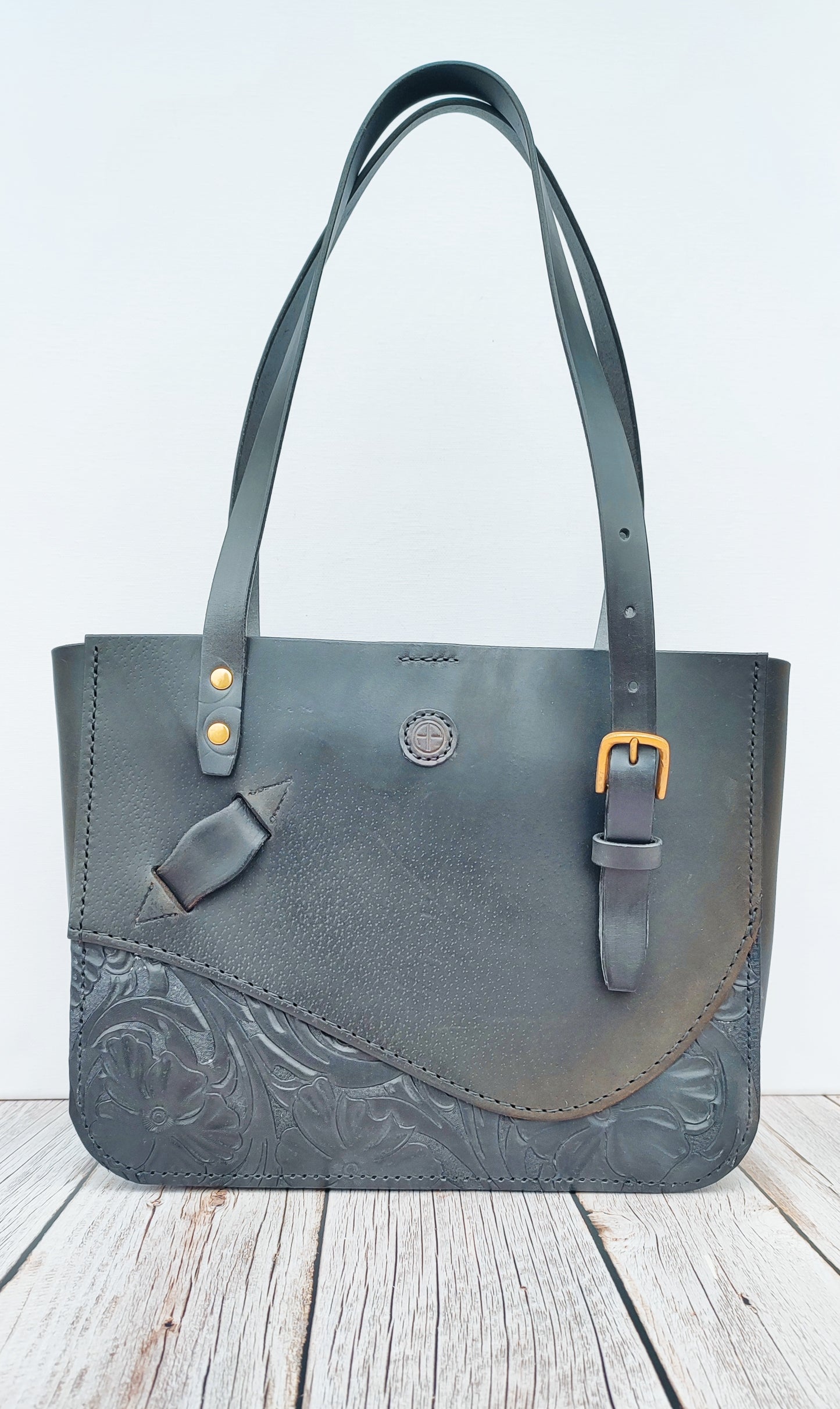 Vue globale du tote bag noir sur un fond neutre. Un sac élégant et sophistiqué avec les nombreux détails rappelant la selle, la briderie, le passant d'étrivière et le cuir sculpté.